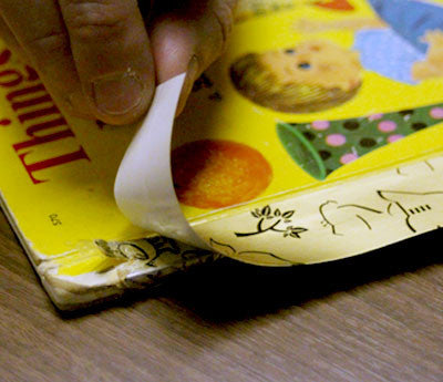 A Gold-Book Repair Tape strip being pressed onto the spine of a Little Golden Book