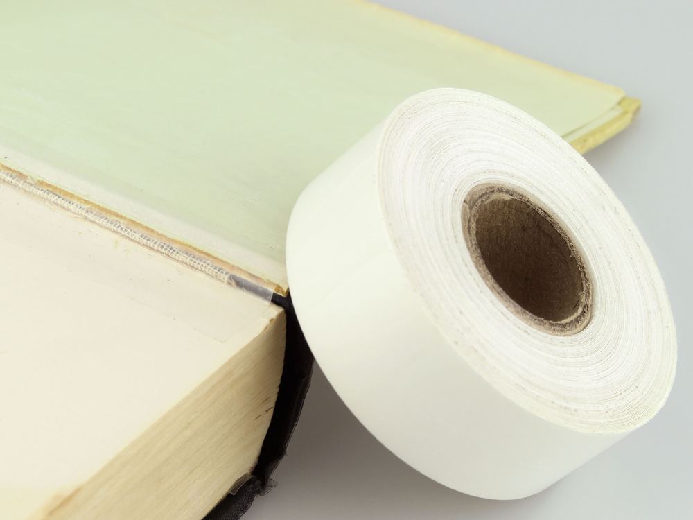 A roll of BookGuard clear stretchable tape beside a repaired spine