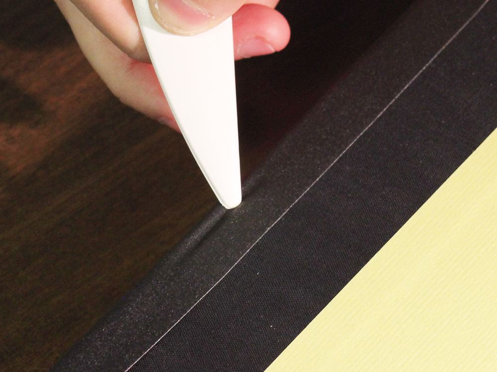 Black BookGuard cloth tape being smoothed along a book's spine