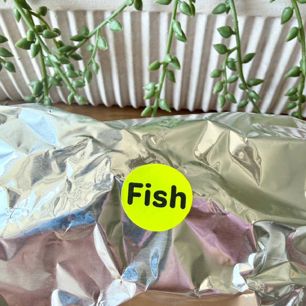 A close-up of crinkled silver foil packaging with a bright yellow circular sticker reading 