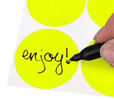 A Person's hand writing the word Enjoy on a sticker with a felt tip marker